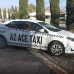 A white taxi parked on the road near four trees